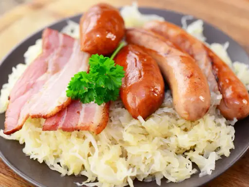 Assiette de choucroute allemande ou alsacienne garnie de saucisses et de lardons, décorée d'une touche de persil frais.
