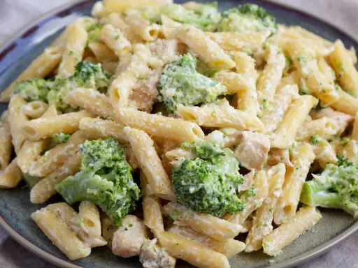 Penne z kurczakiem i brokułami w kremowym sosie, posypane parmezanem. Pyszny makaron z brokułami na talerzu.