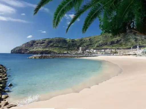 Traumhafter Madeira Strand mit türkisfarbenem Wasser, goldenem Sand und grünen Hügeln im Hintergrund. Palmen spenden Schatten.
