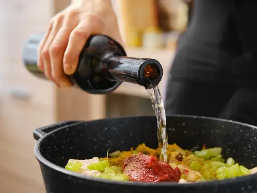 Una mano vierte vino en una sartén con ingredientes. El vino en moderación realza el sabor de la comida.