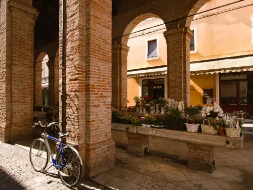 Sotto gli archi di mattoni rossi, un tempo la vecchia pescheria, ora un fiorista espone i suoi colori. Una bicicletta blu riposa sul selciato.