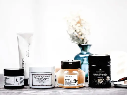 Plusieurs masques pour le visage, dont un masque au miel, sont disposés sur une table en bois.