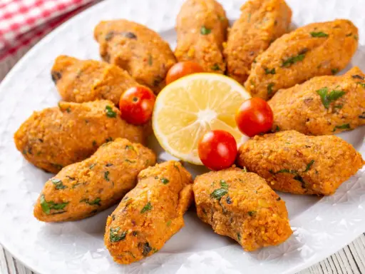 Deliziose polpette di lenticchie, disposte a cerchio su un piatto bianco, con spicchi di limone e pomodorini ciliegino.