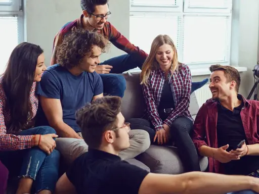 Grupa przyjaciół śmieje się, siedząc na kanapie. Wyglądają, jakby grali w grę, może nawet w Familiadę, odpowiadając na zabawne pytania.