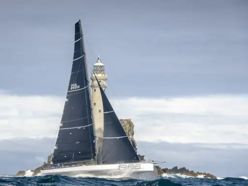 Segelboot mit schwarzen Segeln navigiert durch raue See am Fastnet Rock, ein dramatischer Moment im Fastnet Race.