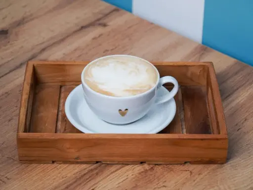 Eine Tasse Kaffee au lait mit Herz-Detail auf einem Holzteller, bereit zum Genießen.