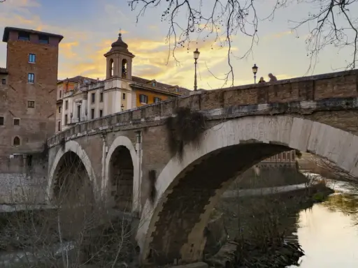 El puente Fabricio, con sus arcos de piedra y la torre medieval, cruza el Tíber bajo un cielo anaranjado.