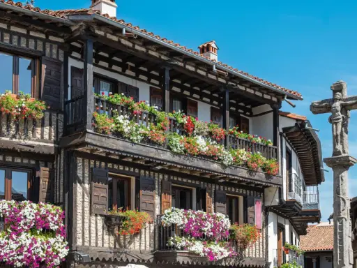 Casas de madera y piedra adornadas con flores en la Sierra de Francia. Un crucero de piedra se alza en la plaza.