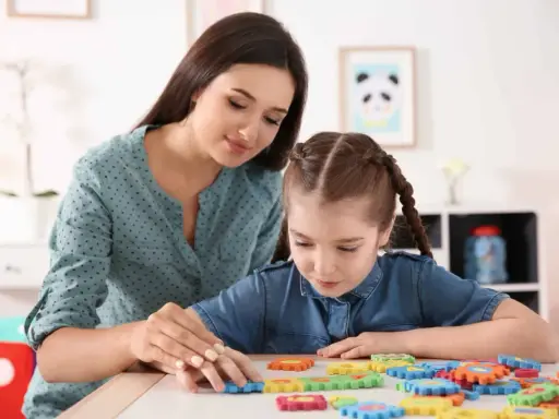 Terapeuta pomaga dziecku z niepełnosprawnością intelektualną układać kolorowe puzzle.