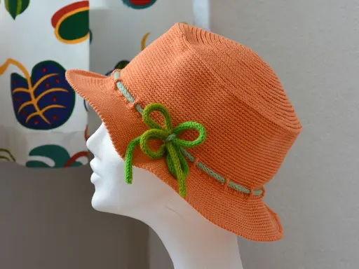En orange virkad hatt med ljusgröna detaljer och en rosett. Perfekt för sommaren!