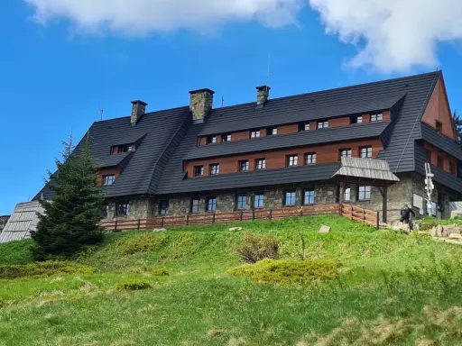 Schronisko na Turbaczu, cel wielu tras rowerowych i pieszych. Kamienno-drewniany budynek na zielonym wzgórzu.