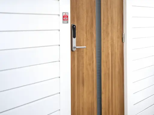 En modern ytterdörr med ett Verisure Yale Doorman V2N lås. Dörren är i trä och har en vitmålad panelvägg bredvid.