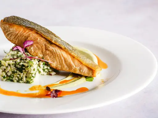 Wykwintna fotografia jedzenia: soczysty łosoś z chrupiącą skórką, podany na kaszy z ziołami i kremowym puree.