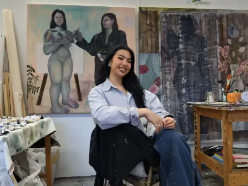 A young woman, one of many talented gen z artists, smiles in her studio, surrounded by her evocative paintings.