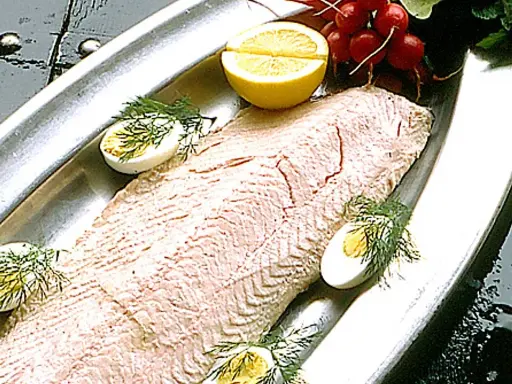 En vacker inkokt lax serveras på ett silverfat med citronklyftor, kokta ägg och dill.
