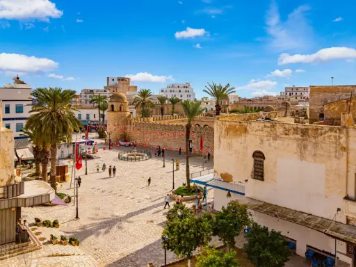 Tunezja Sousse czy warto? Rynek z palmami, zabytkową wieżą i flagami. Słoneczny dzień zachęca do zwiedzania.