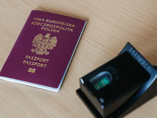 Polski paszport i czytnik linii papilarnych na drewnianym blacie.