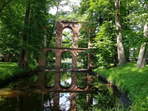 Ruiny mostu z cegły nad kanałem, otoczone zielenią. Idealne na weekendowe wycieczki, to jedne z fajnych miejsc niedaleko Warszawy.