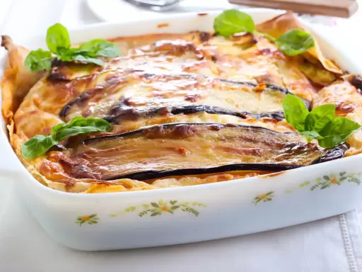 Parmigiana di melanzane napoletana recién horneada, dorada y burbujeante, decorada con hojas de albahaca fresca.