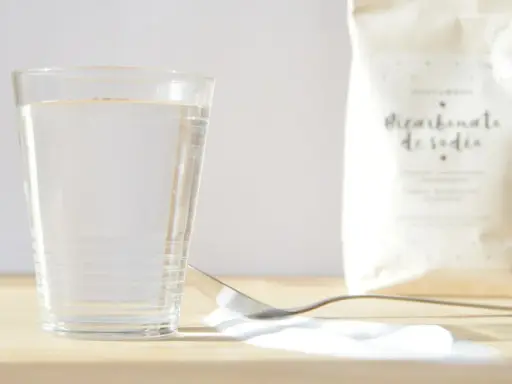 Un vaso de agua, una cuchara con bicarbonato y una bolsa de bicarbonato de sodio. ¡Listo para mezclar con vinagre!