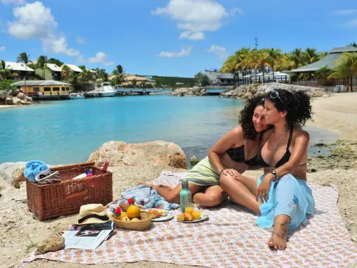 Two women enjoy a picnic on a beach in Curacao, a gay-friendly paradise.
