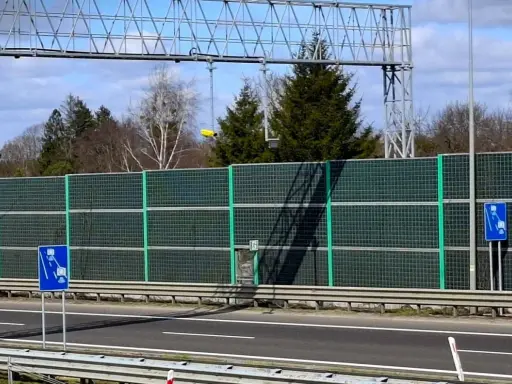 Znak drogowy informujący o odcinkowym pomiarze prędkości na tle ekranów akustycznych i drzew.