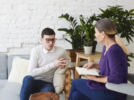Mężczyzna w okularach rozmawia z kobietą, która notuje. Wyglądają jak na sesji z coachem psychologiem.