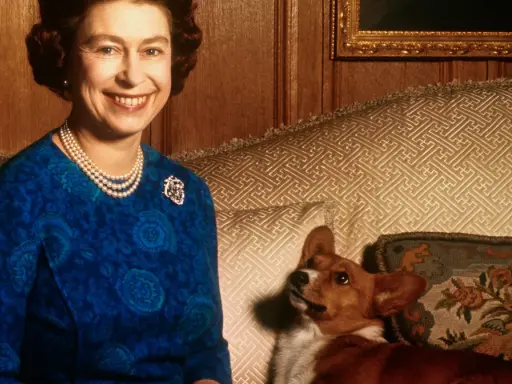 Królowa Elżbieta uśmiecha się, siedząc obok swojego wiernego psa rasy corgi.