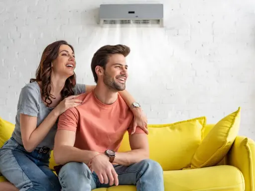 Couple souriant sur un canapé jaune, profitant de la brise fraîche d'un climatiseur moins de 50 db.