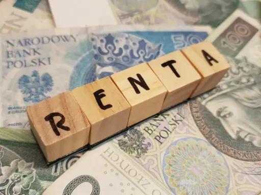 Drewniane klocki z napisem "RENTA" leżą na polskich banknotach.