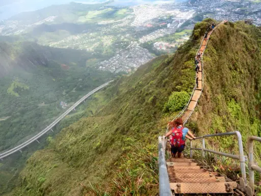 Wanderer erklimmen die "Stairway to Heaven" in Hawaii, eine steile Treppe mit atemberaubendem Blick auf die Stadt und die Natur.
