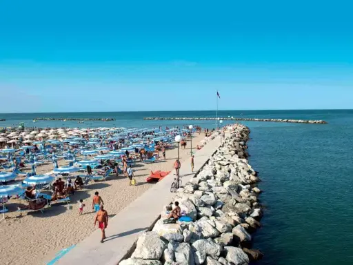 Spiaggia affollata a Gatteo Mare Cesenatico, con ombrelloni, lettini e persone che passeggiano sul molo.