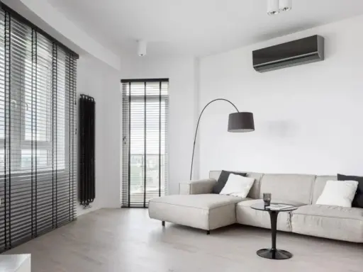 Unità interna di climatizzatore su parete bianca, con divano e lampada. Ideale per capire la differenza tra monosplit e dualsplit.