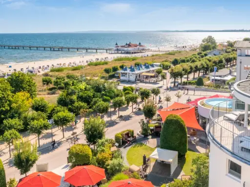Blick auf Strandpromenade mit Seebrücke, Ostsee und Hotelterrasse mit Pool.