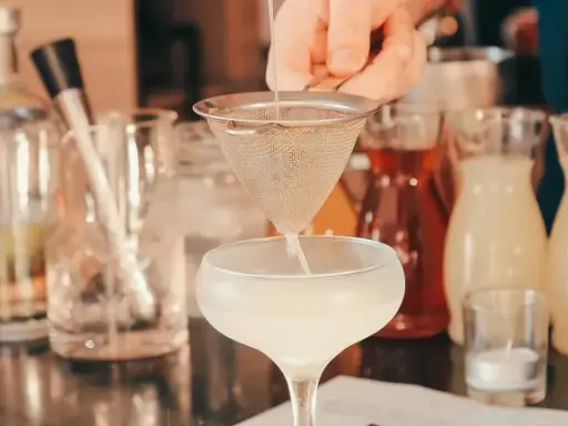 Ile napojów na wesele 80 osób? Barman przygotowuje drinka, w tle butelki z alkoholami i syropami.