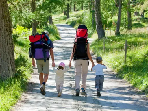 Familia con mochilas camina por un sendero boscoso, ideal para rutas para hacer con niños.