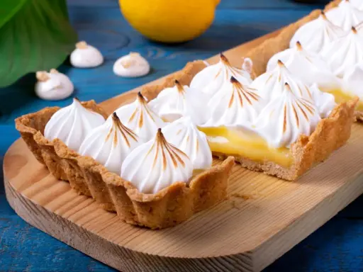 Tarta de limón con abundante merengue suizo tostado, sobre una tabla de madera.