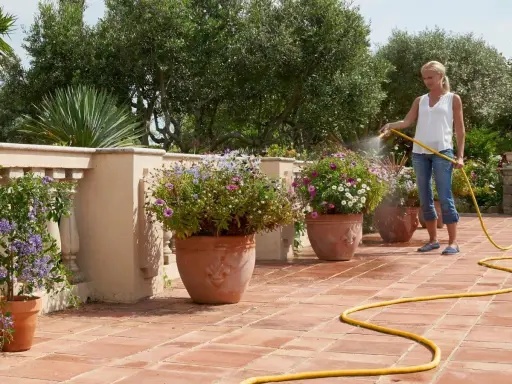 Mujer riega flores en macetas en una terraza, mostrando diferentes tipos de riego para mantenerlas sanas y vibrantes.