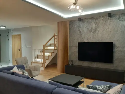 Nowoczesny salon z szarą ścianą, telewizorem i drewnianymi lamelami. Zobacz, z czym łączyć lamele, by stworzyć przytulne wnętrze.