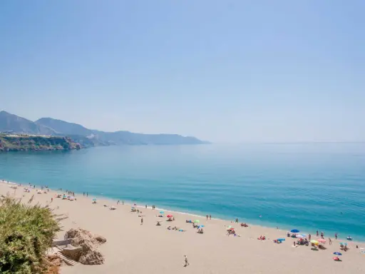 Sonniger malaga strand mit vielen Menschen, die sich unter bunten Sonnenschirmen entspannen. Das türkisfarbene Meer lädt zum Baden ein.