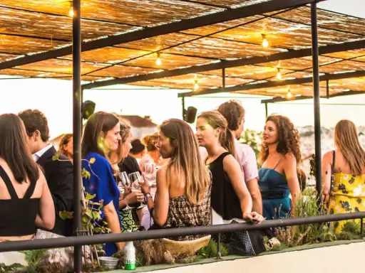 Menschen genießen den Abend auf einer Dachterrasse in einem **bar lissabon**. Unter einem Strohdach mit Lichterketten unterhalten sie sich bei Getränken.