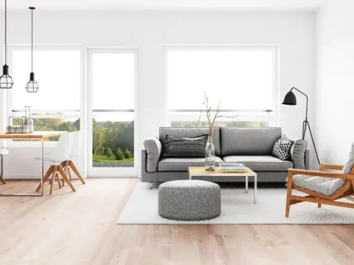 Elegante salón comedor con sofá gris, mesa de centro y sillas blancas. La iluminación es clave para combinar lamparas salon comedor, con colgantes sobre la mesa y una lámpara de pie.