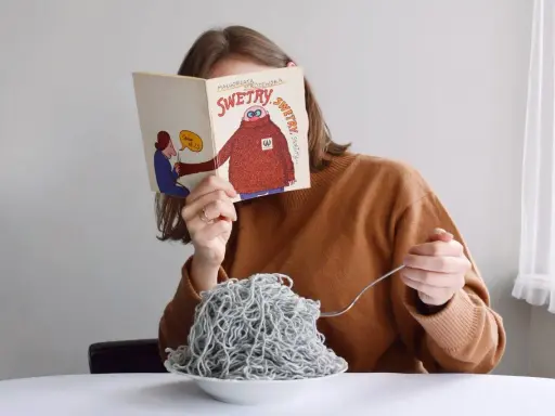 Dziewczyna czyta książkę o swetrach, jedząc spaghetti z włóczki. Jak znaleźć początek włóczki?