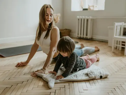 Mama uczy dziecko nauki oddychania podczas ćwiczeń jogi. Dziecko leży na poduszce w kształcie rekina, a mama w pozycji kobry.