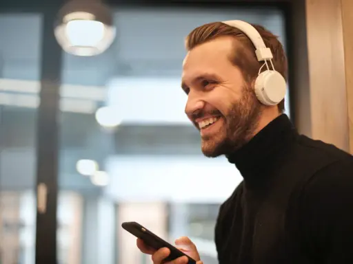 Uśmiechnięty mężczyzna w słuchawkach na uszach trzyma telefon. Proste jak podłączyć słuchawki przewodowe do telefonu Samsung.
