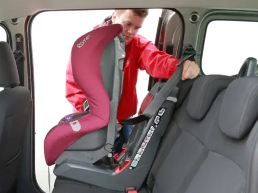 Mężczyzna montuje fotelik samochodowy. Sprawdź, jak sprawdzić, czy samochód ma isofix, patrząc na zaczepy fotelika.