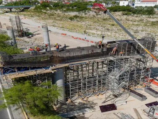Obreros trabajan en la construcción de puentes de acero, con grúas y andamios rodeando las estructuras.