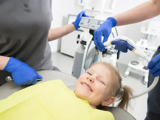 Uśmiechnięta dziewczynka na fotelu dentystycznym, przygotowywana do zabiegu z użyciem sedacji wziewnej.