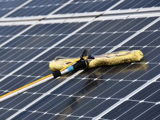 Reinigung von Solaranlagen mit einem Teleskopwischer. Gelber Wischerkopf auf dunklen Solarzellen.