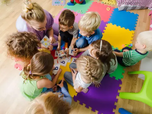 Dzieci i nauczycielka bawią się kartami z literami, ucząc się alfabetu. Ciekawe zajęcia w przedszkolu.